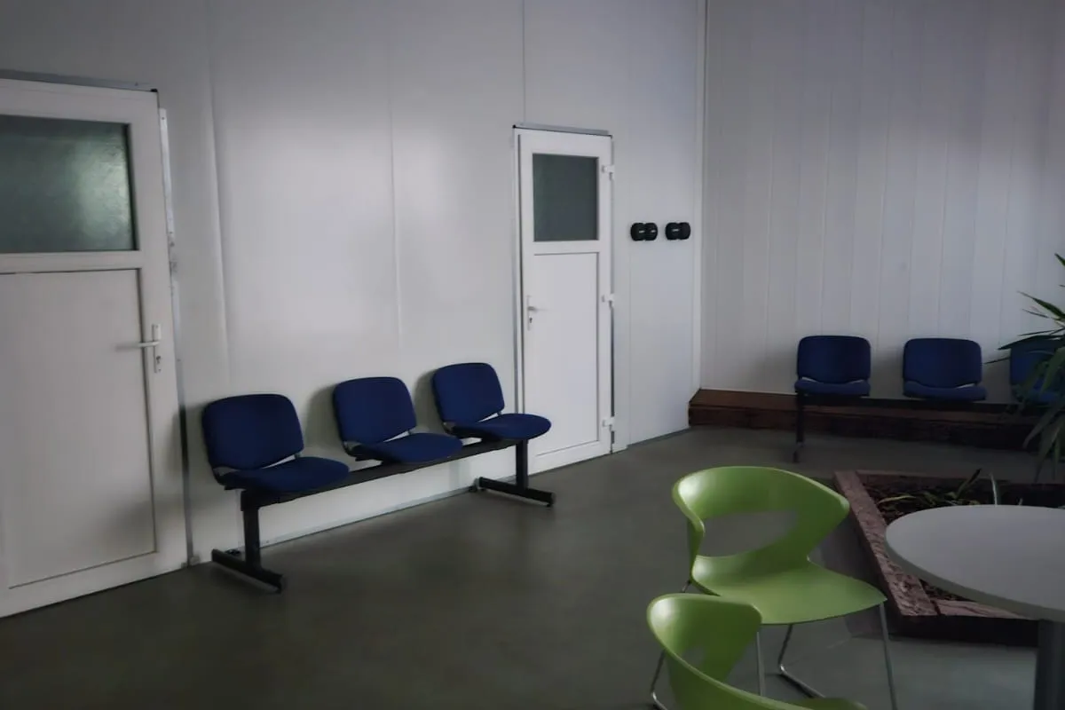 L’espace d’attente du hall, avec ses rangées de sièges bleus et une table entourée de chaises vertes.